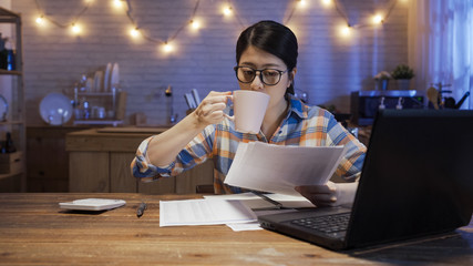 elegant asian korean woman drinking cup of coffee and working with home finances at dining table in...
