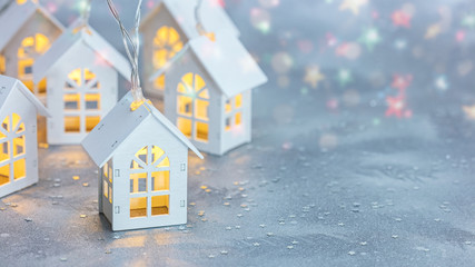 white christmas lights in form of toy wooden houses on festive silver background with confetti