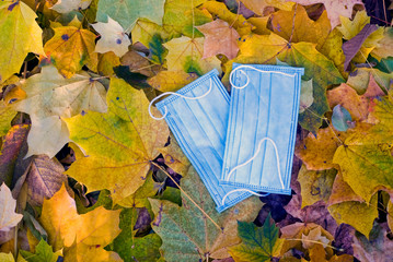 A medical mask for protection against viruses, lies on yellow, fallen leaves