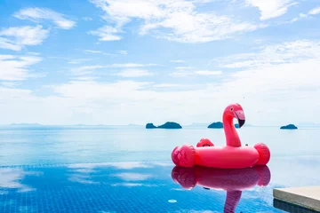 Zelfklevend Fotobehang Beautiful outdoor swimming pool in hotel resort with flamingo float around sea ocean white cloud on blue sky © siraphol