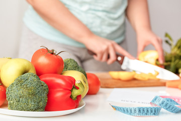 Cooking Meal. Chubby girl standing in kitchen cutting vegetables ingredients and tape measure close-up blurred background
