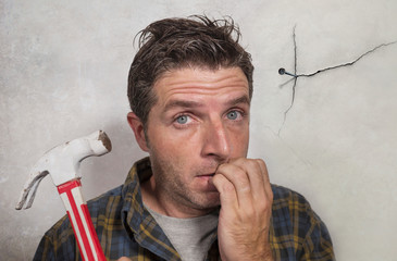 man holding hammer driving a nail for hanging a frame but making funny faces for the  mess cracking...
