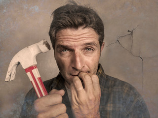 man holding hammer driving a nail for hanging a frame but making funny faces for the  mess cracking...