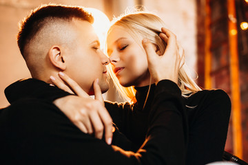 Close up portrait of a lovely young man and woman while man is touching his girlfriend hair before kiss against a light.