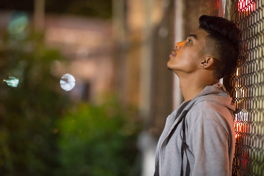 Sad Young Asian Man Leaning On Fence In The City Streets At Night