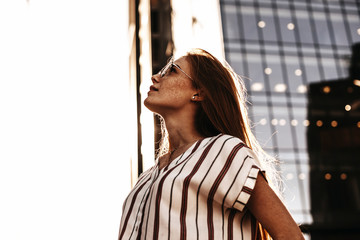 Fototapeta premium Side view portrait of a lovely red haired woman with freckles looking up seriously against modern business.