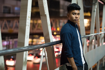 Young Asian man leaning on the footbridge at night