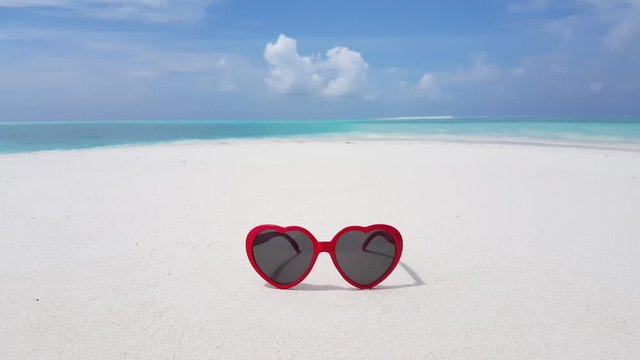 Red heart-shaped sunglasses in the center of a bright wallpaper with ocean and clouds background in Haiti