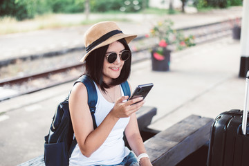 Obraz premium Travel and vacation concept,Happy asian woman tourist using cell phone and waiting train at train station