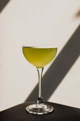 A yellow alcoholic drink in a cocktail nick and nora glass. Direct sunlight.