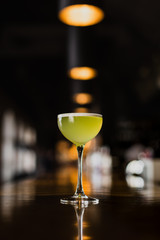 A yellow alcoholic drink in a cocktail nick and nora glass at the bar counter. Selected focus.