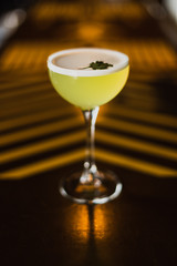A yellow alcoholic drink in a cocktail nick and nora glass at the bar counter. Selected focus.