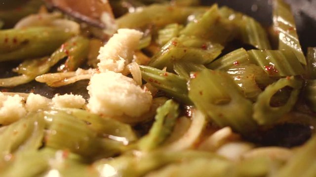 Chef fries an edible burdock with spices in a pan.