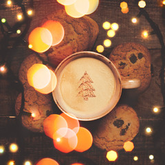 Christmas coffee cup with tree shape on foam and cookies with New Year’s garland and lights on a...