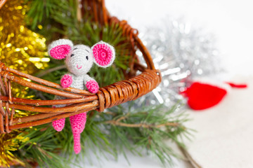 Obraz premium new year's sivmole 2020 a gray mouse with pink ears crocheted lies in a wicker wooden basket with green spruce branches, in the background is gold and silver tinsel
