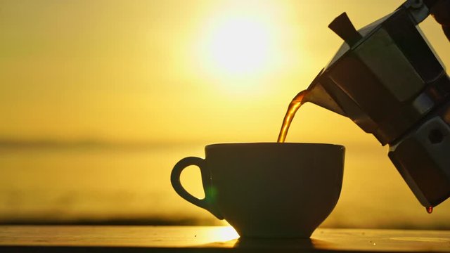 man pouring coffee from moka pot beside the lake in the morning with sunrise background