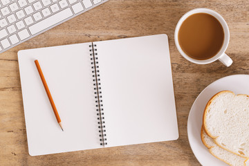  Top view of the office table On the table there are notebook, coffee cup, bread, pencil and keyboard.