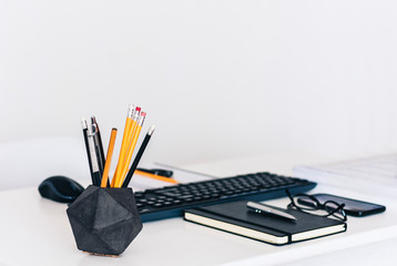modern workplace: white table, keyboard laptop computer, concrete holder with pencils and pens,...