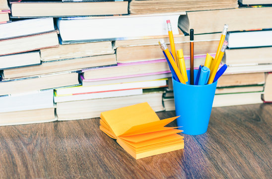 Colorful pencils in blue plastic holder and orange note paper, stack of books education back to school background, with copy space for text.
