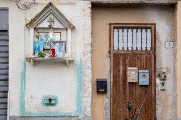 Palermo, Italy, September 19, 2019: Detail of a facade of a house with a wooden door and a small altar with images of the Virgin Mary and Catholic cross