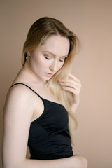 Fototapeta premium Graceful young woman in a black top posing against beige wall.