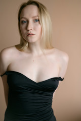 Graceful young woman in a black top posing against beige wall.