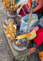 Street food, roasted yellow corn or maize. Local lady vendor roasting corn on the simmering coal fire and serving it with lemon and salt, Northeast, Shillong, Meghalaya, India