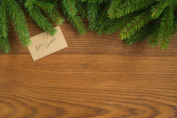 Flat lay christmas background with spruce twigs and merry christmas card on ash wood surface