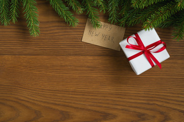 Flat lay christmas background with spruce twigs and white gift box with red ribbon on ash wood surface