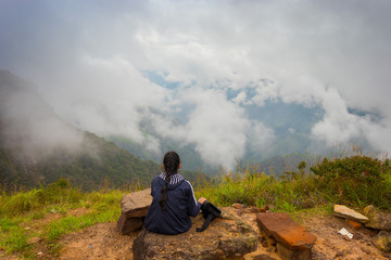 Obraz premium Lost in the clouds. The young girl with braided hair is taking a rest after hiking in the magnificent lush green mountain valley covered with forest and clouds, Shillong, Northeast, Meghalaya, India