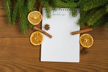 Flat lay christmas gift list notepad with spruce twigs and decorations on ash wood surface