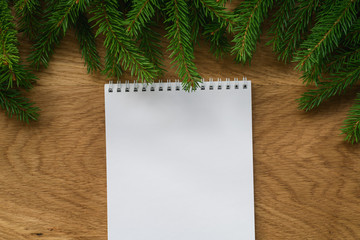 Flat lay empty notepad with spruce twigs on oak wood surface