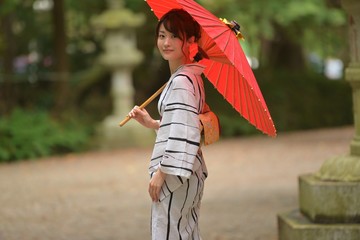 和傘を手に神社の境内で微笑む浴衣を着た若く美しい日本人女性