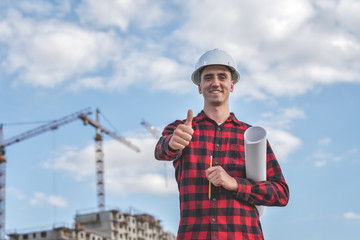 civil engineer in a white helmet on the background of construction, with a raised thumb.