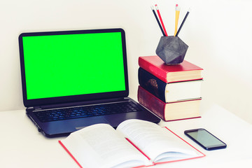 Green screen laptop, smartphone, notebook and pencils in concrete holder on white table, education office concept background.