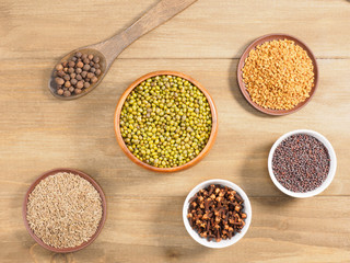 Allspice, mung bean, mustard seeds, fenugreek, cumin, cloves on brown wooden background. Indian...
