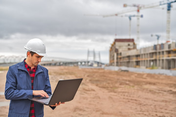 civil engineer in a white helmet looking documents on the background of construction