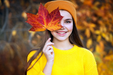 Beautiful girl walking outdoors in autumn. Smiling girl collects yellow leaves in autumn.