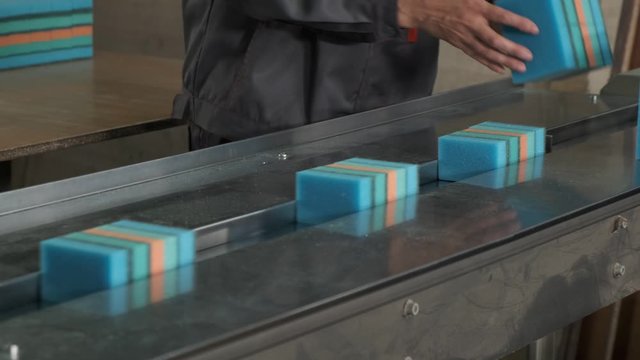 Dusty line of conveyor for production of sponges for washing dishes, worker neatly lays out batches of products, packaging of goods, low-professional production, household goods, paralon articles