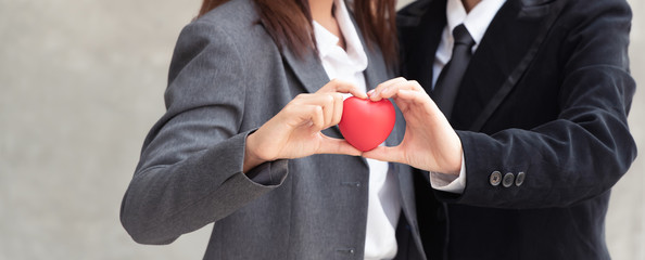 Happy business couple people holding red heart together.