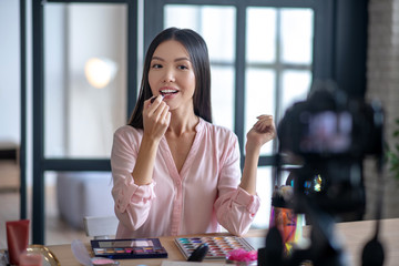 Blogger putting lipstick while filming makeup tutorial