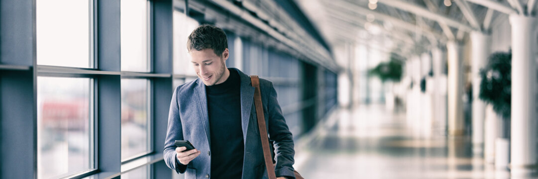 Business man texting on mobile phone at airport on business trip using cellphone texting sms message on smartphone app - young businessman commuter lifestyle panoramic banner.