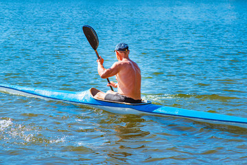 Man paddling a blue and yellow kayak on the river near the shore. Kayaking concept.A man swims in a...