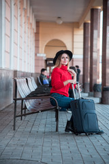 Obraz na płótnie Canvas Beautiful train station landscape with a pretty lady with a suitcase on retro chairs on the train station platform. Vintage style. (expectation, happiness, sadness, purpose, escape - concept)