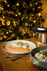 Wiener Würstchen und Kartoffelsalat als typisches Weihnachtsessen zu Heiligabend in Deutschland am Weihnachtsbaum mit Weihnachtsdekoration und Lichterketten