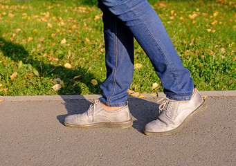 Close up of a woman legs walking in an autumn park on asphalt trail in sunny day; healthy lifestyle, activity concept
