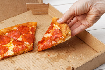 Closeup slice of italian pepperoni pizza in hand and open box with pizza leftovers