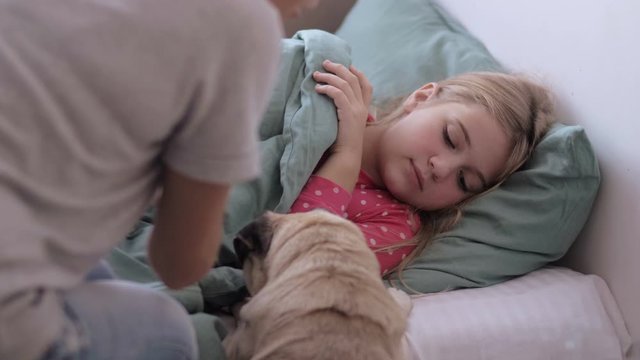 Mother caring for sick child lying in bed with flu measuring temperature using thermometer, girl with fever lying with a cute dog on the sofa at home, Family Treatment