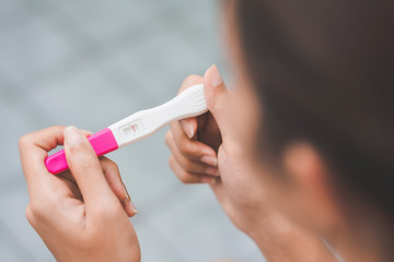 Unhappy young asian woman holding pregnancy test showing a negative result in her bathroom,...