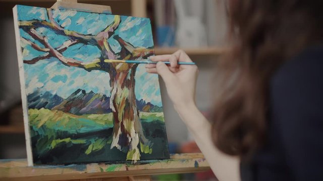 Artist woman is painting by oil paints in studio, canvas fixing on easel